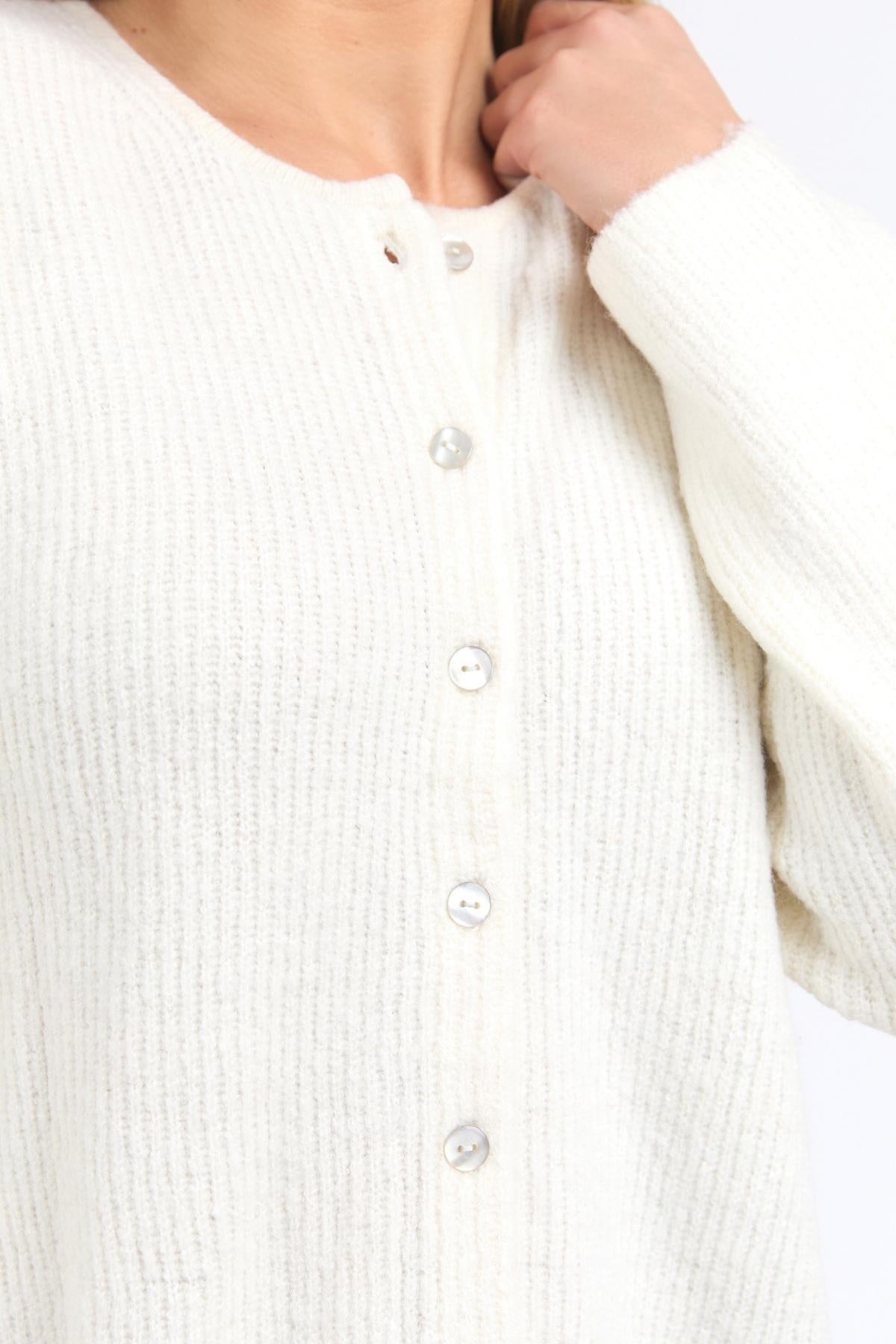 A person wears the Foxwood Murphy Knit Cardi—a textured, white, long-sleeved cardi with a relaxed fit—shown from shoulders to waist, with one hand touching their neck.
