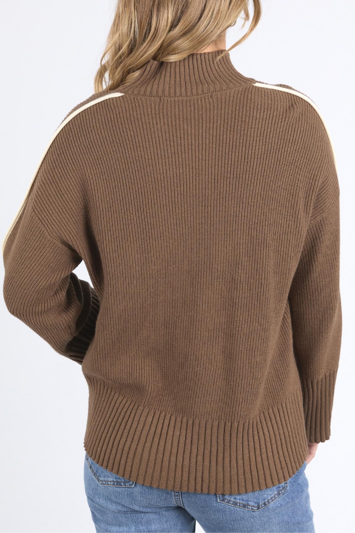 A person with long, light brown hair is shown from the back, wearing the Foxwood Oliver Knit, a relaxed-fit sweater featuring a mock neck and cream shoulder stripes, paired with blue jeans.