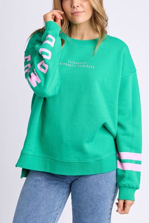 A woman sports a relaxed-fit Foxwood Origin Crew fleece in bright green with pink sleeve stripes, "MOOD" in pink, white chest text, and blue jeans.