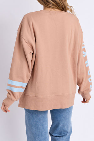 A person is seen from the back in a loose, light brown Foxwood Origin Crew sweatshirt with blue sleeve stripes and light blue jeans, against a plain white background, highlighting the relaxed-fit fleece's contemporary design.
