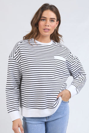 A woman in the Foxwood Original Stripe Crew, a relaxed fit jumper with cuffed sleeves, pairs it with light blue jeans and stands with one hand on her hip, facing the camera against a plain light background.