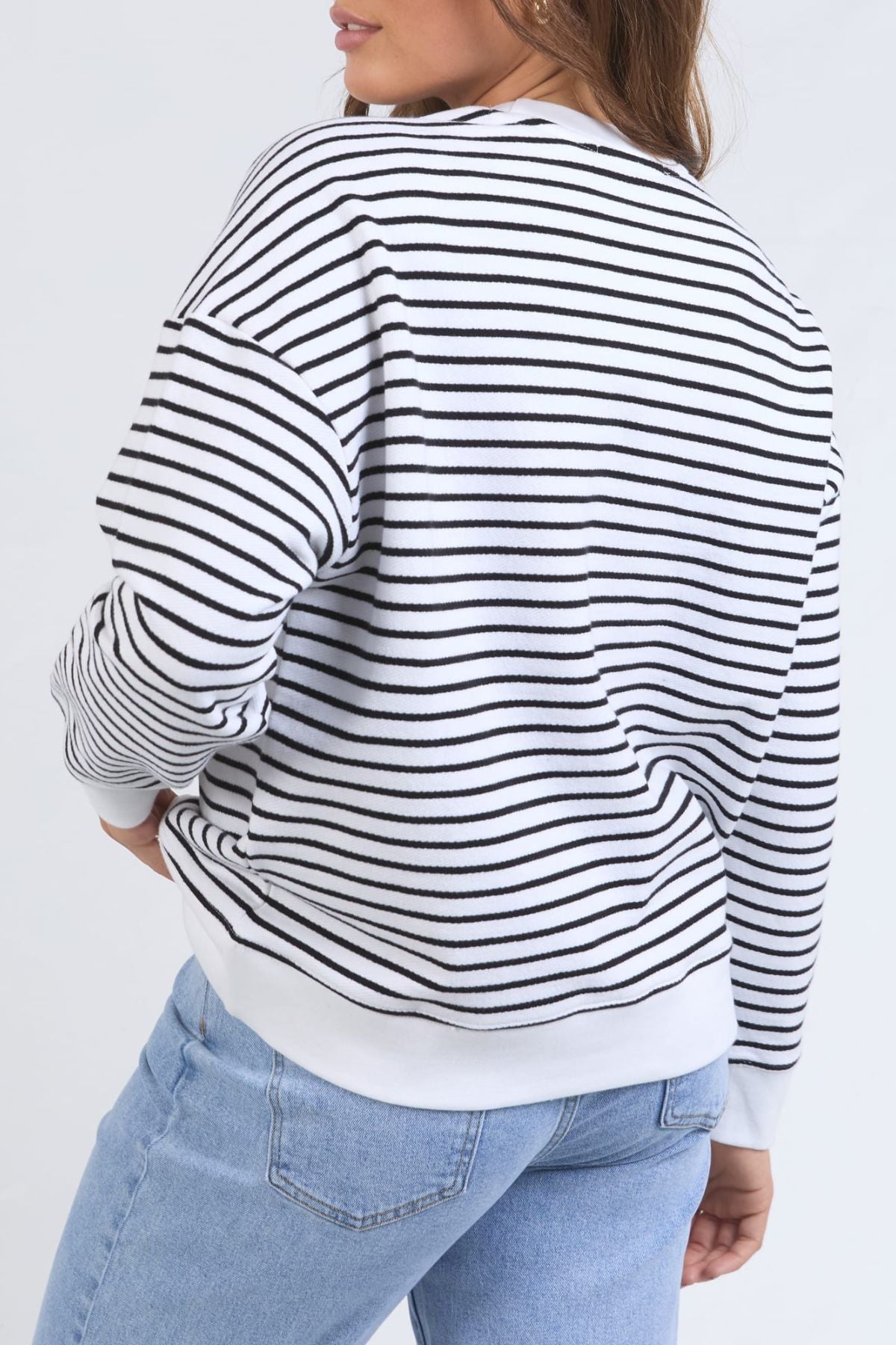 A woman models the Foxwood Original Stripe Crew, a relaxed-fit black and white striped jumper, with light blue jeans. She stands with one hand on her hip against a plain background—ideal for stylish winter outfits.