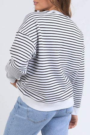 A woman models the Foxwood Original Stripe Crew, a relaxed-fit black and white striped jumper, with light blue jeans. She stands with one hand on her hip against a plain background—ideal for stylish winter outfits.