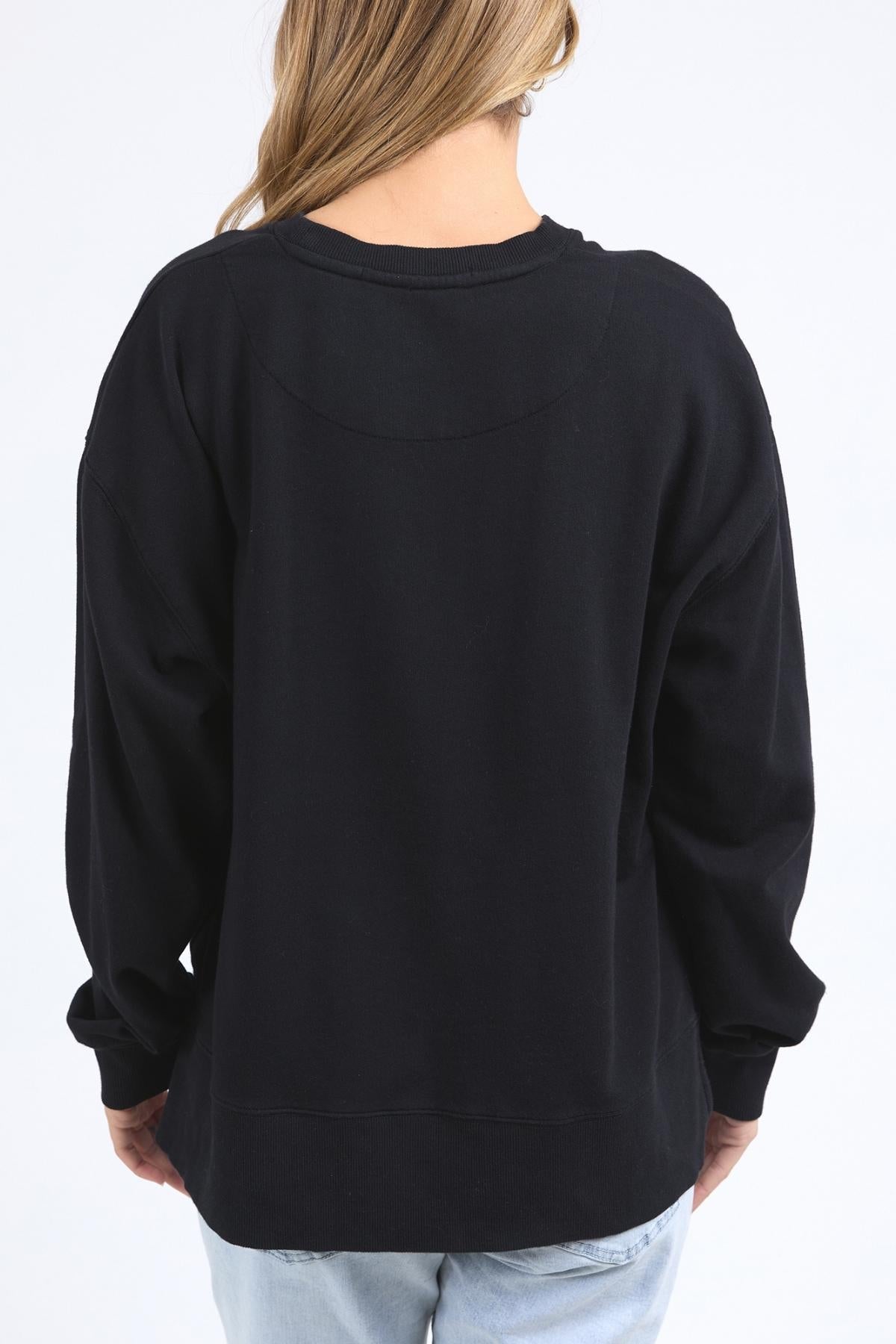 A person with long, light brown hair stands with their back to the camera wearing the Foxwood Posy Crew—check the half chest measurement for sizing—paired with light blue jeans, set against a plain white background.