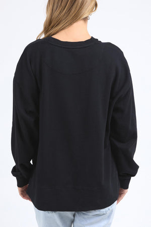 A person with long, light brown hair stands with their back to the camera wearing the Foxwood Posy Crew—check the half chest measurement for sizing—paired with light blue jeans, set against a plain white background.