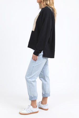 A woman stands sideways against a white background, wearing the Foxwood Posy Crew with light blue cuffed jeans and white sneakers. For sizing, check the half chest measurement or contact our customer service team for help.