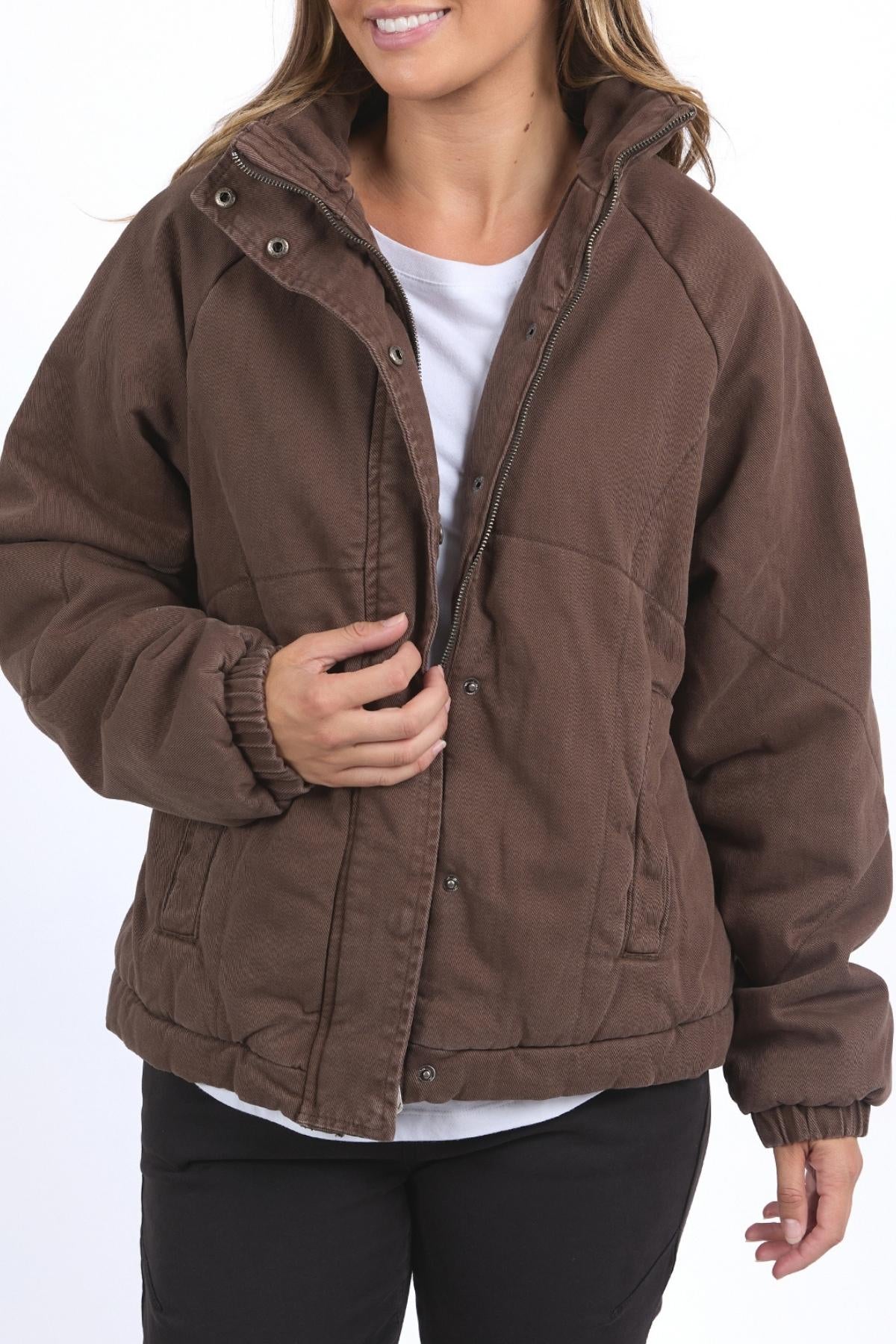 A person models the Foxwood Rosalee Jacket—a brown, cropped slouch style—over a white shirt and black pants, standing against a plain white background and smiling while partially unzipping the jacket.