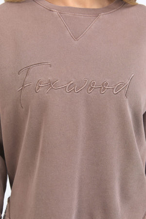 A close-up of the Foxwood Signature Crew, a 100% cotton crewneck sweater in mauve with "Foxwood" embroidered in cursive on the chest.