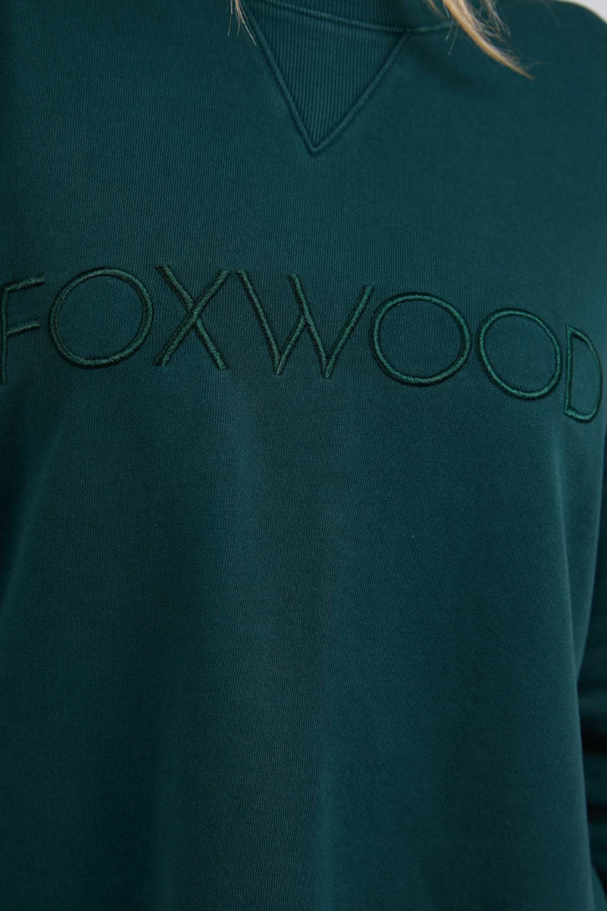 Close-up of the Foxwood Simplified Crew, a dark green 100% cotton sweatshirt with "FOXWOOD" embroidered in matching green across the chest.