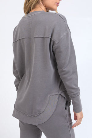 A person wears a relaxed fit Foxwood Simplified Crew sweatshirt with exposed seams and grey pants, standing with their back to the camera against a plain light background.