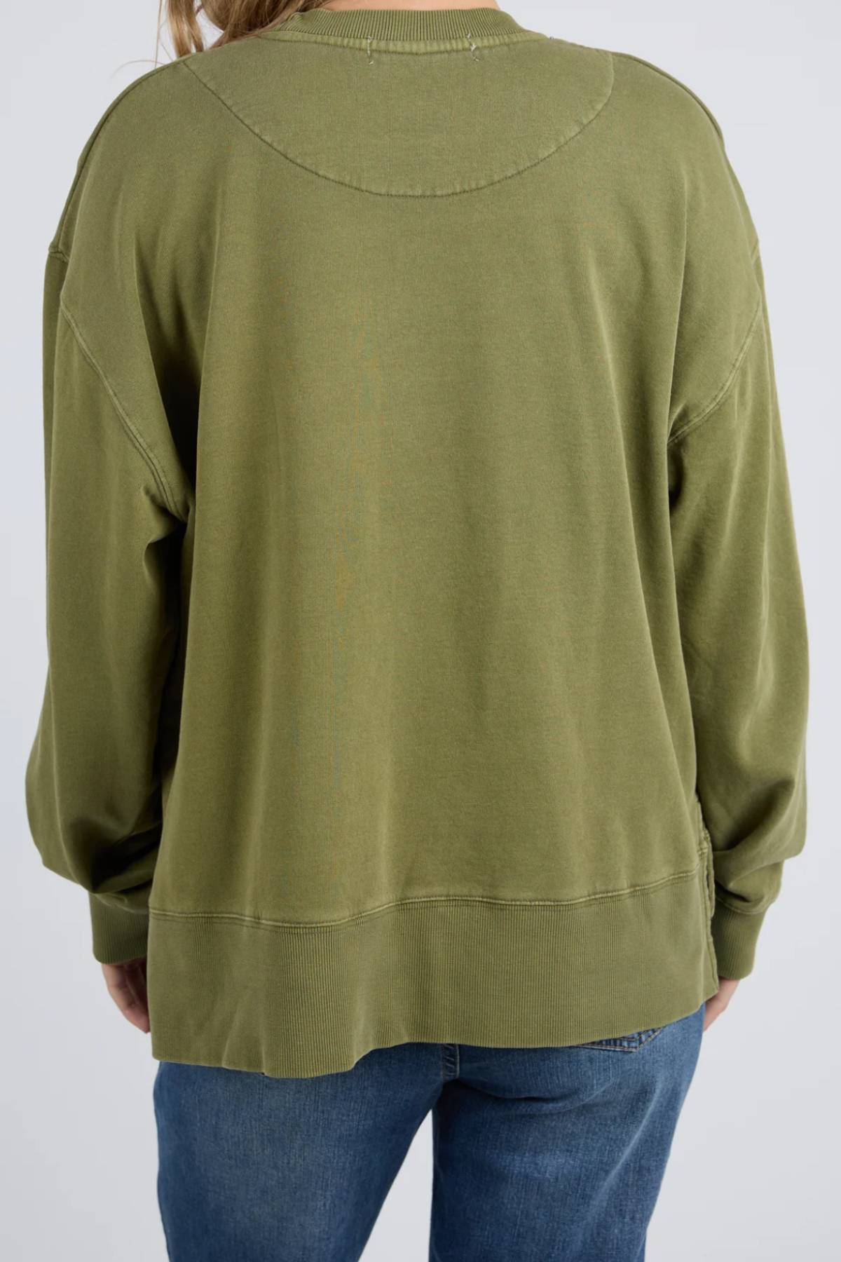Model wears the Foxwood Trademark Crew—an olive green, relaxed-fit top in unbrushed cotton fleece—paired with blue jeans. Shown from the back against a plain backdrop, it’s an easy choice for casual style.