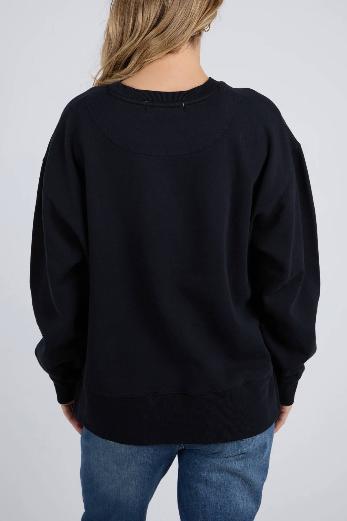 A person with long, light brown hair wears a loose-fitting Foxwood Trademark Crew and blue jeans, facing away from the camera against a plain light background—a comfortable essential for any casual wardrobe.