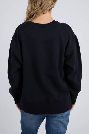 A person with long, light brown hair wears a loose-fitting Foxwood Trademark Crew and blue jeans, facing away from the camera against a plain light background—a comfortable essential for any casual wardrobe.