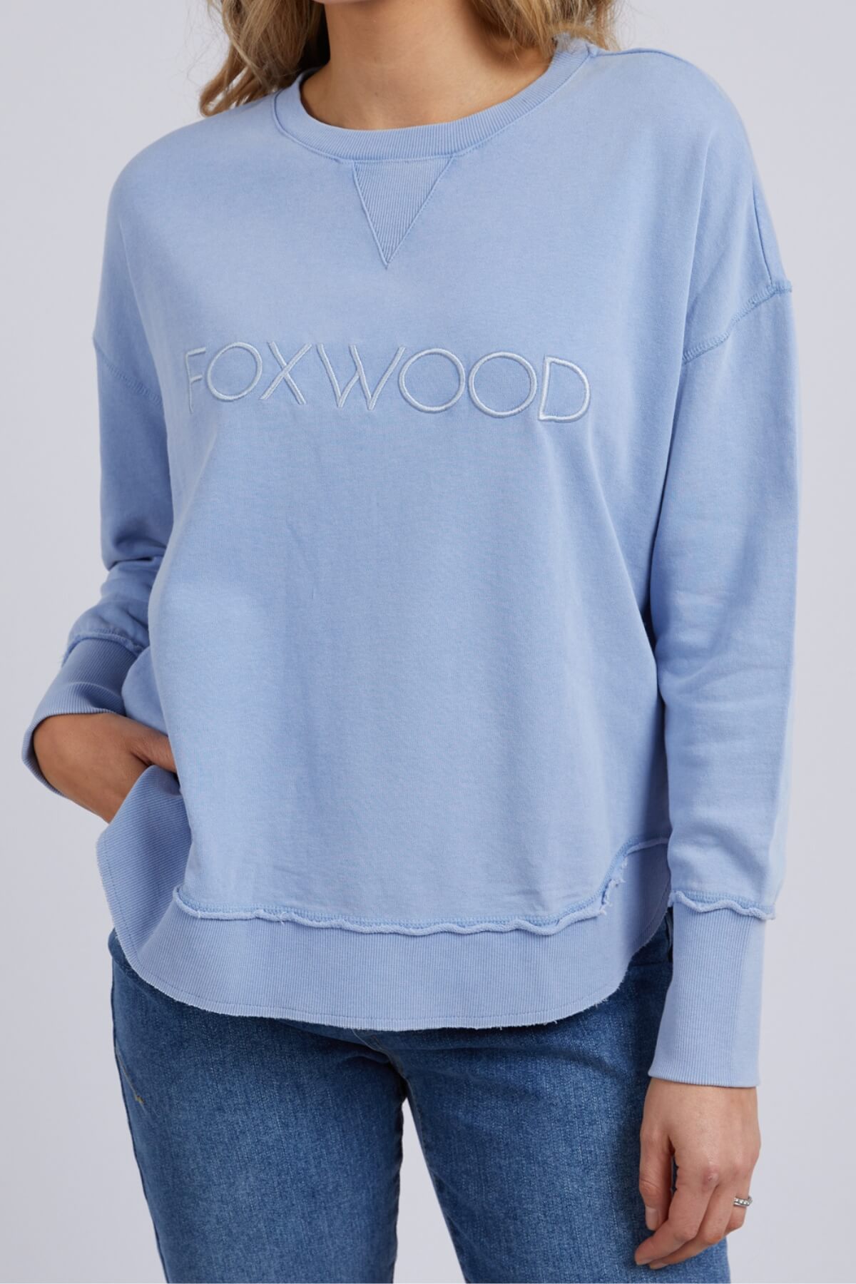 Sporting the light blue Foxwood Washed Simplified Crew with "FOXWOOD" embroidery, an individual pairs it with blue jeans. With one hand in their pocket, this 100% cotton piece remains the centerpiece of an effortlessly cool look.