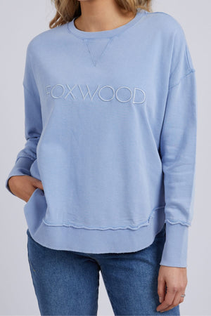 Sporting the light blue Foxwood Washed Simplified Crew with "FOXWOOD" embroidery, an individual pairs it with blue jeans. With one hand in their pocket, this 100% cotton piece remains the centerpiece of an effortlessly cool look.