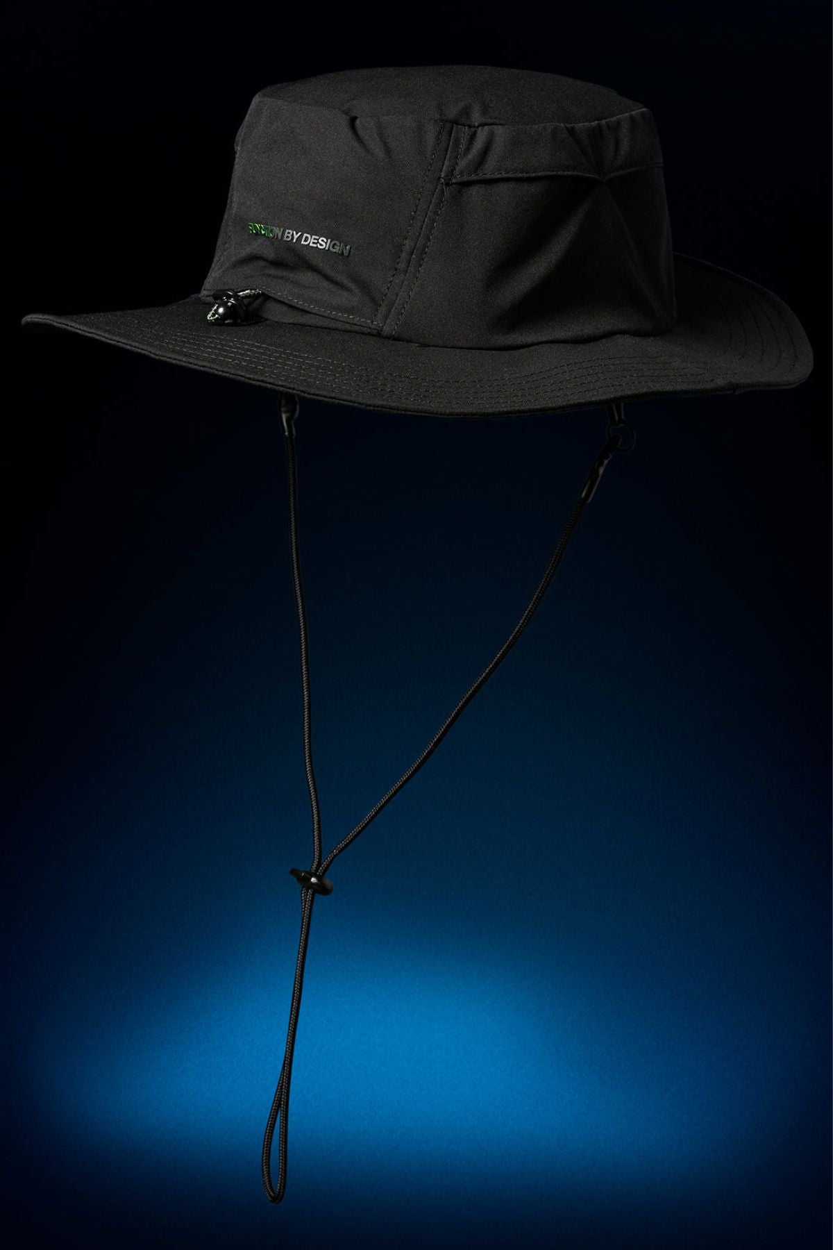 The FXD CP-14 Boonie Hat, a black wide-brim hat with chin strap, pocket, and subtle “DESIGN BY DESIGN” text on the front, is shown against a dark blue gradient—ideal for outdoor work and sun protection.