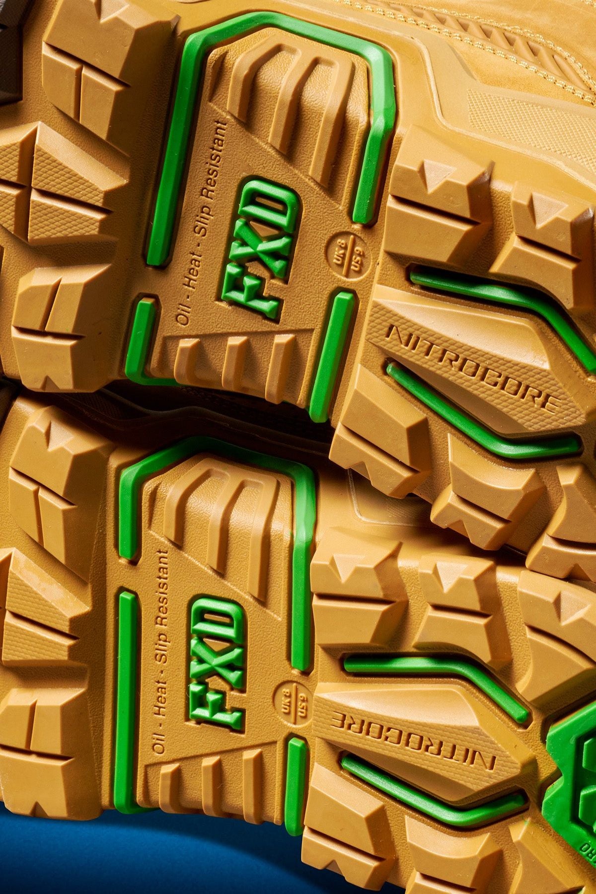 Close-up of the yellow and green treaded soles of FXD Dura X-1 Nitrocore™ High Cut, High Performance Work Boots, with "FXD," "NITROCORE," and "Oil, Heat, Slip Resistant" embossed on the bottom.