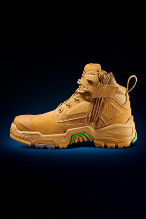 The FXD Dura X-2 Nitrocore™ Mid Cut High Performance Work Boots feature a tan, rugged design with a thick textured sole, side zipper, and reinforced toe, showcased against a dark gradient background with a subtle blue glow.