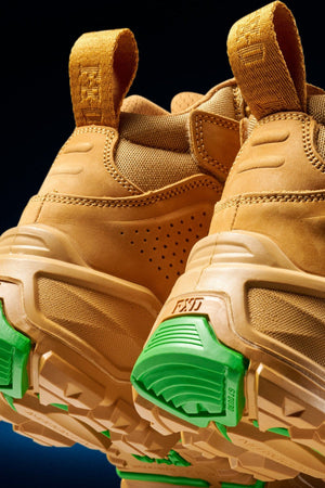 Close-up of the back and soles of FXD Dura X-2 Nitrocore™ Mid Cut High Performance Work Boots, featuring textured beige uppers, yellow pull tabs, chunky tan outsoles, and bright green accents on the heel and tread.