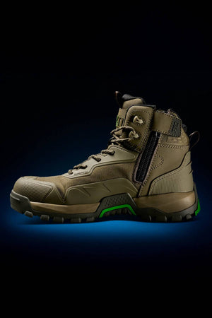 The FXD WB-6 Work Boot, a rugged brown boot with a synthetic upper, black and green accents, side zipper, and thick tread sole, is displayed against a dark background illuminated by a blue light glow underneath.