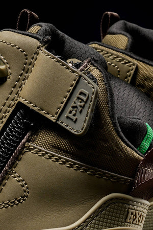 Close-up of the FXD WB-6 Work Boot, featuring a rugged olive-green design with brown and black accents, visible stitching, a synthetic upper, side zipper, and an "FXD" tag near the ankle.