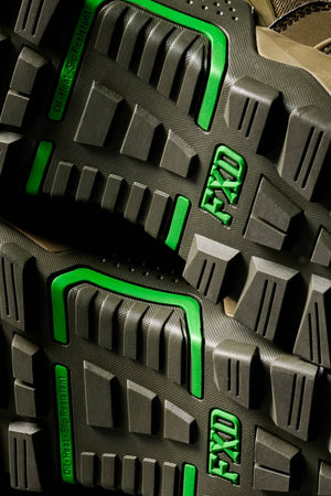 Close-up of the FXD WB-6 Work Boot’s rugged black soles with bold green accents and "FXD" molded into the tread. Deep grooves and angular shapes provide traction, meeting high safety standards.