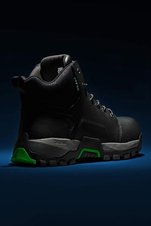 The FXD WB-3 Work Boot is a robust black footwear option made from premium leather. It features green accents on the sole and heel, presented in a rear view. The boot is illuminated against a dark background, emphasizing its durable design and textured sole.