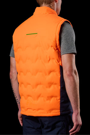 Seen from the back against a black background, a person wears the FXD WO-6 Hi Vis Insulated Puffer Vest in bright orange over a gray short-sleeve shirt, showcasing their left forearm tattoo.