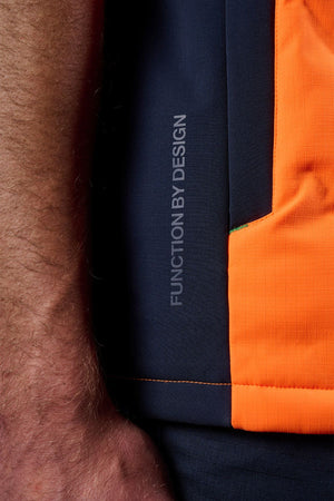 Close-up of a person's arm beside the FXD WO-6 Hi Vis Insulated Puffer Vest in bright orange, featuring water-repellent fabric and "FUNCTION BY DESIGN" printed vertically.