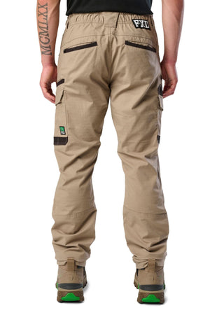 A person stands facing away, wearing FXD WP-12 durable work pants with dark brown pocket accents, green-soled boots, utility pockets, a waistband patch reading “FXD,” and a green logo on the side pocket.