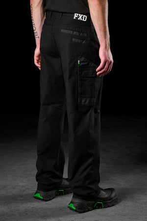 A person stands facing away, wearing black FXD WP-3L Loose Fit Stretch Canvas Work Pants with multiple pockets and "FXD" near the waistband. They also wear black shoes with green accents, against a plain dark background.