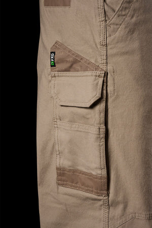 Close-up of a cargo pocket on FXD WP-3L Loose Fit Stretch Canvas Work Pants, showing detailed stitching, a flap with black and green tag, and reinforced edges against a solid black background.
