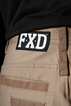 Close-up of FXD WP-3L Loose Fit Stretch Canvas Work Pants in tan, featuring a black and white FXD label on the waistband. They’re styled with a tucked-in black shirt, highlighting their durability and comfortable fit.