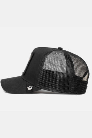 Side view of a Goorin Bros The Lone Wolf Cap, a black trucker cap with mesh back panels and solid fabric front, featuring an emblem patch and a small sticker on the brim's side, set against a plain light background.