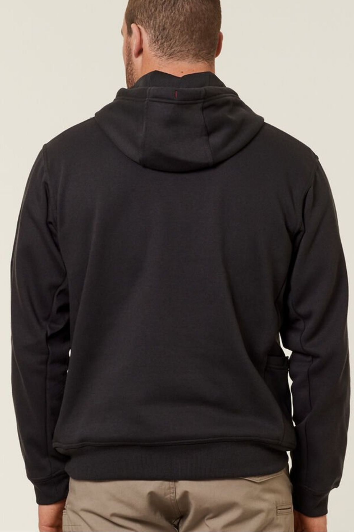 A person wearing a Hard Yakka Plain Fleece Hoodie in black and beige pants is shown from behind. The relaxed-fit hoodie has its hood down, set against a plain, off-white background.