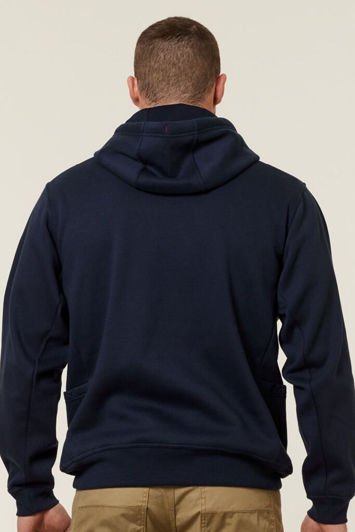 Rear view of a person wearing a Hard Yakka Plain Fleece Hoodie in navy and beige pants. The hooded, brushed fleece provides comfort and warmth against a neutral, light background.