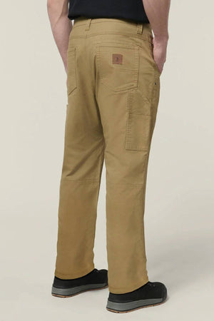 Shown from the back against a plain light background, a person stands with hands in pockets, wearing black shoes and Hard Yakka Heritage Carpenters Pant—demonstrating classic workwear style.