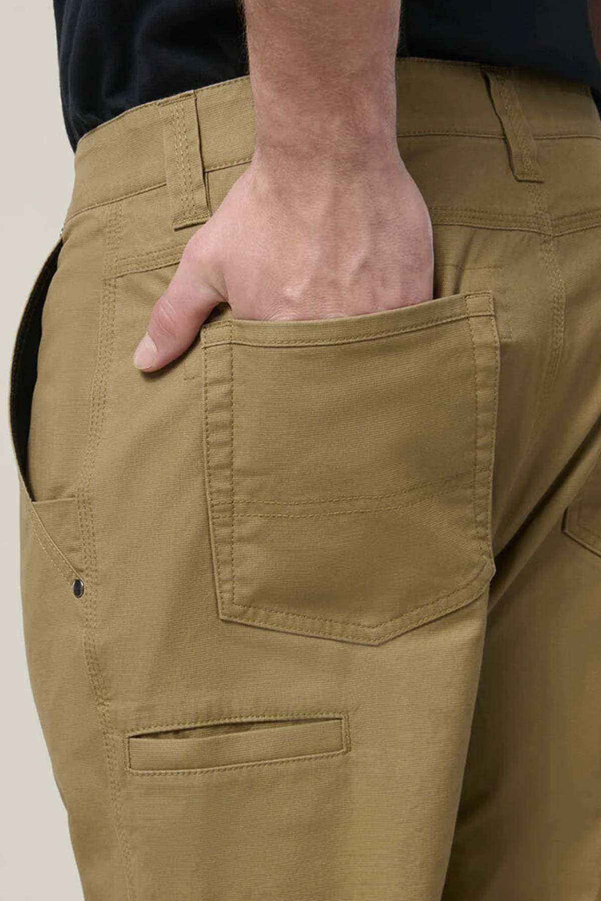 Wearing the Hard Yakka Heritage Carpenters Pant, a person stands with their right hand partly tucked into the back pocket, showcasing the stitching and classic workwear details of this iconic piece.