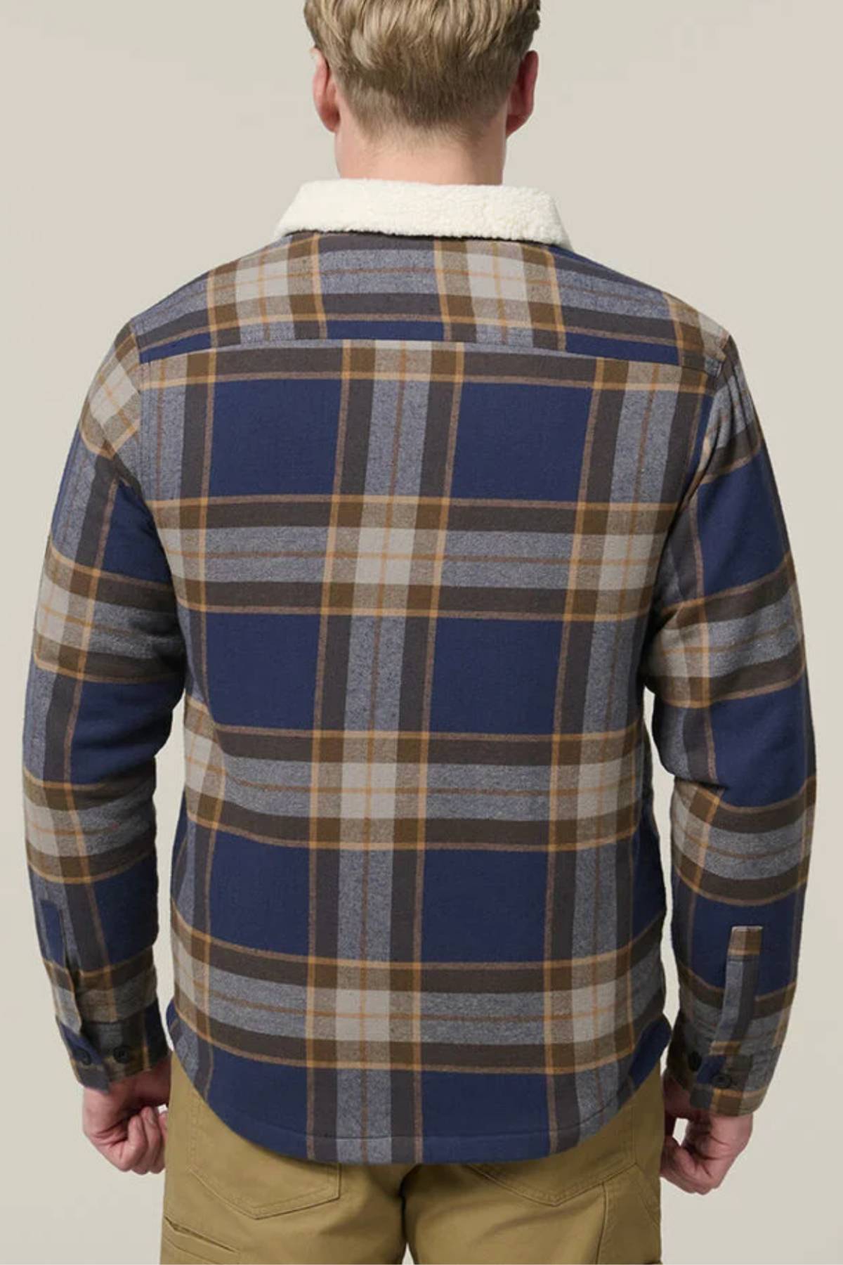 A person with short blond hair is seen from the back wearing a blue, gray, and brown plaid Hard Yakka Heritage Trucker Sherpa Jacket with a white collar and beige pants, standing against a plain light background—ideal for winter.