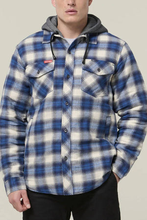A person wears the Hard Yakka Quilted Flannelette Shacket in blue and white plaid, featuring front buttons and chest pockets, layered over a gray hoodie. Hands are in pockets, ready for winter.