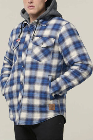 A person stands against a plain background, hands in pockets, wearing a blue and white plaid Hard Yakka Quilted Flannelette Shacket over a gray hoodie. The shacket features black buttons, a chest pocket, and warm quilted flannelette.