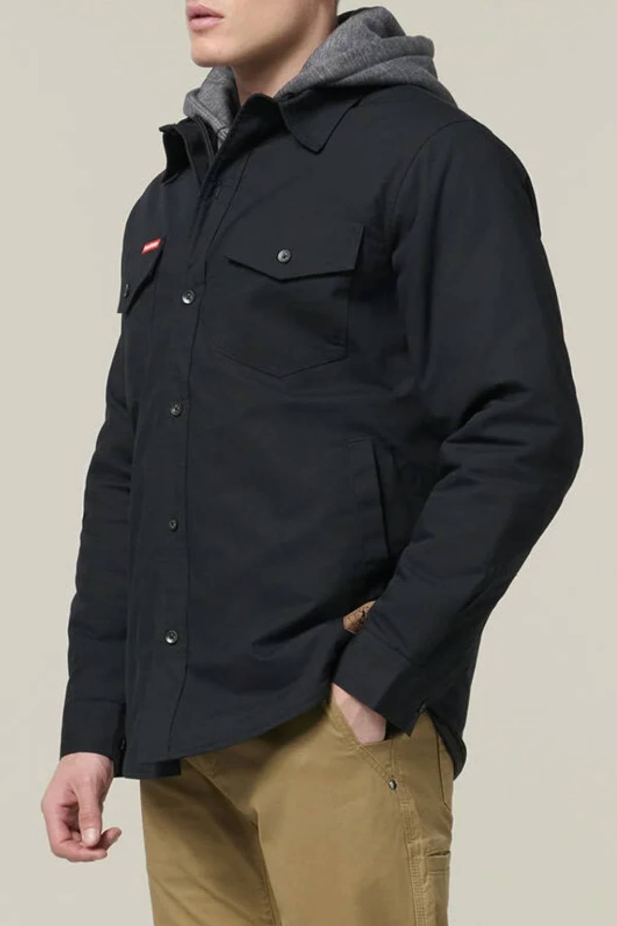 A person stands against a plain background wearing the Hard Yakka Quilted Solid Shacket over a gray hooded sweatshirt and tan pants, one hand in their pocket.