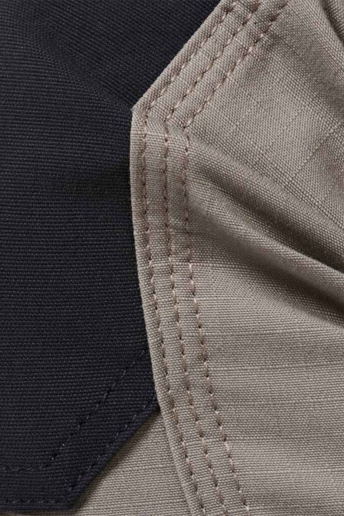 A close-up view of the Hard Yakka Raptor Pant's two-toned fabric with visible stitching. One section features black material, while the other is gray. The seam where these two fabrics meet stands out, showcasing intricate stitching and texture on both sides—exemplary craftsmanship you'd expect from the Hard Yakka Raptor Pant line.