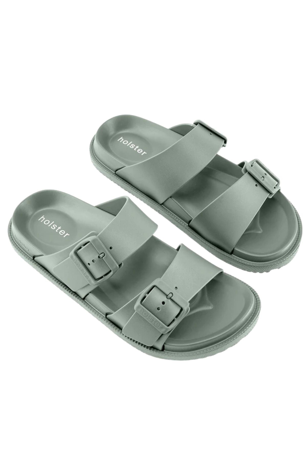 Holster Soleseeker: Light green vegan slide sandals with two adjustable buckle straps, textured soles, and "holster" branding on the footbeds, shown on a white background.