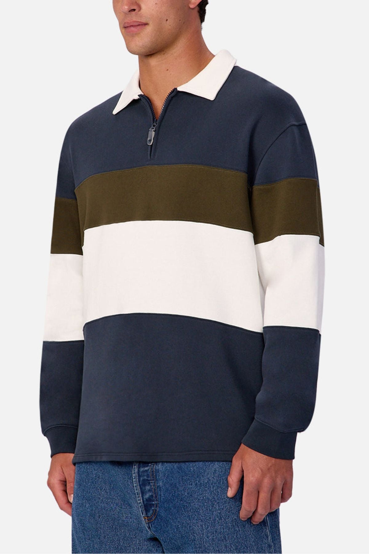 A man wearing the Industrie The Stanstead Tracktop, a contemporary color-blocked pullover with navy, olive green, and white stripes plus a half-zip collar, paired with blue jeans—perfect for casual style.