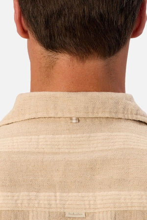 The image shows the back of a person’s neck and head, wearing the Industrie The Ardenza Short Sleeve Shirt in beige. This shirt features a textured fabric, a camp collar, short sleeves, and a small loop detail at the upper back below the collar.