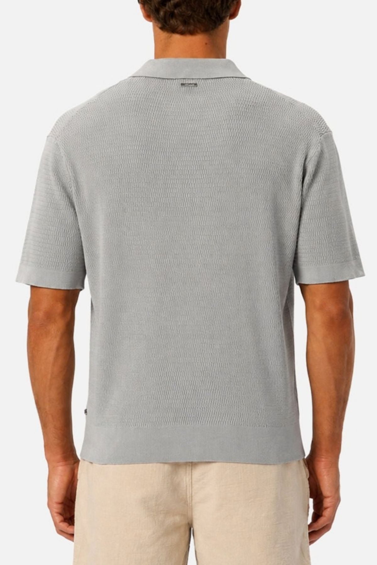 A man is shown from behind, wearing the Industrie The Bastien Polo in light gray, which features a classic collar and refined, textured fabric. He pairs it with beige shorts against a plain white background.