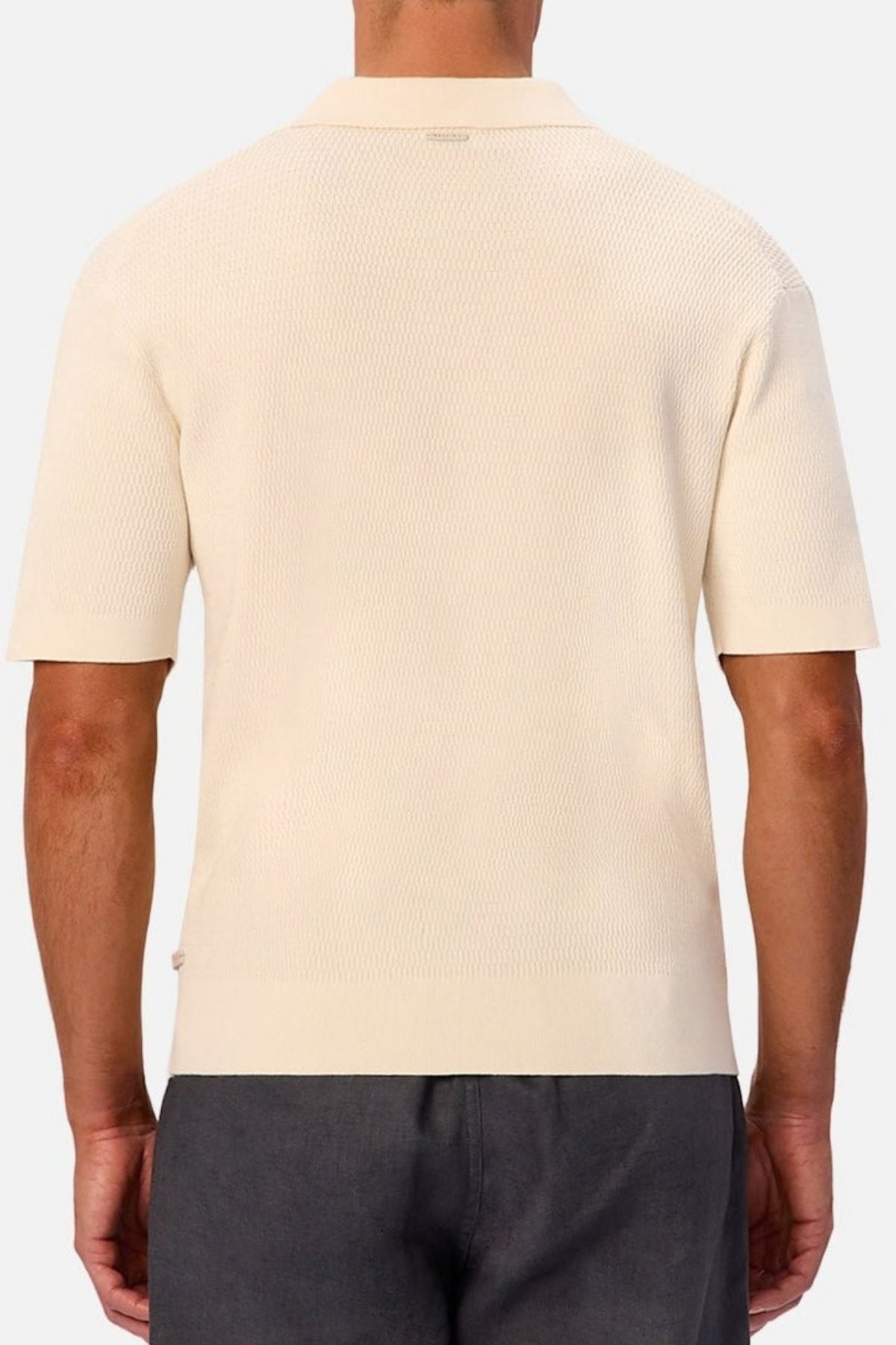 A person is shown from the back against a plain background, wearing the Industrie The Bastien Polo in short sleeves with a classic collar and textured cream-colored fabric, paired with dark gray pants.