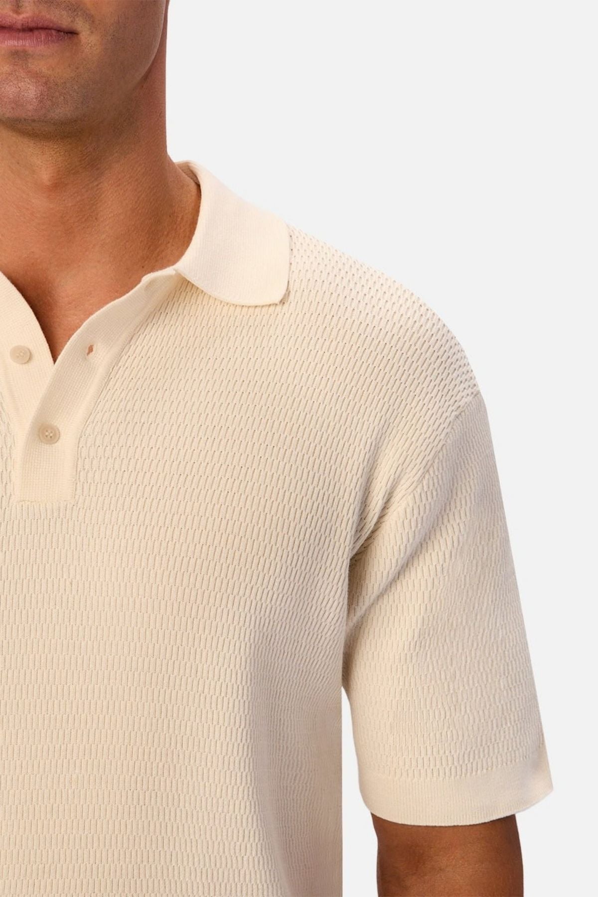 A man wearing the Industrie The Bastien Polo—a textured, short-sleeve, cream-colored shirt with a classic collar—is shown from the chest up against a plain light background.
