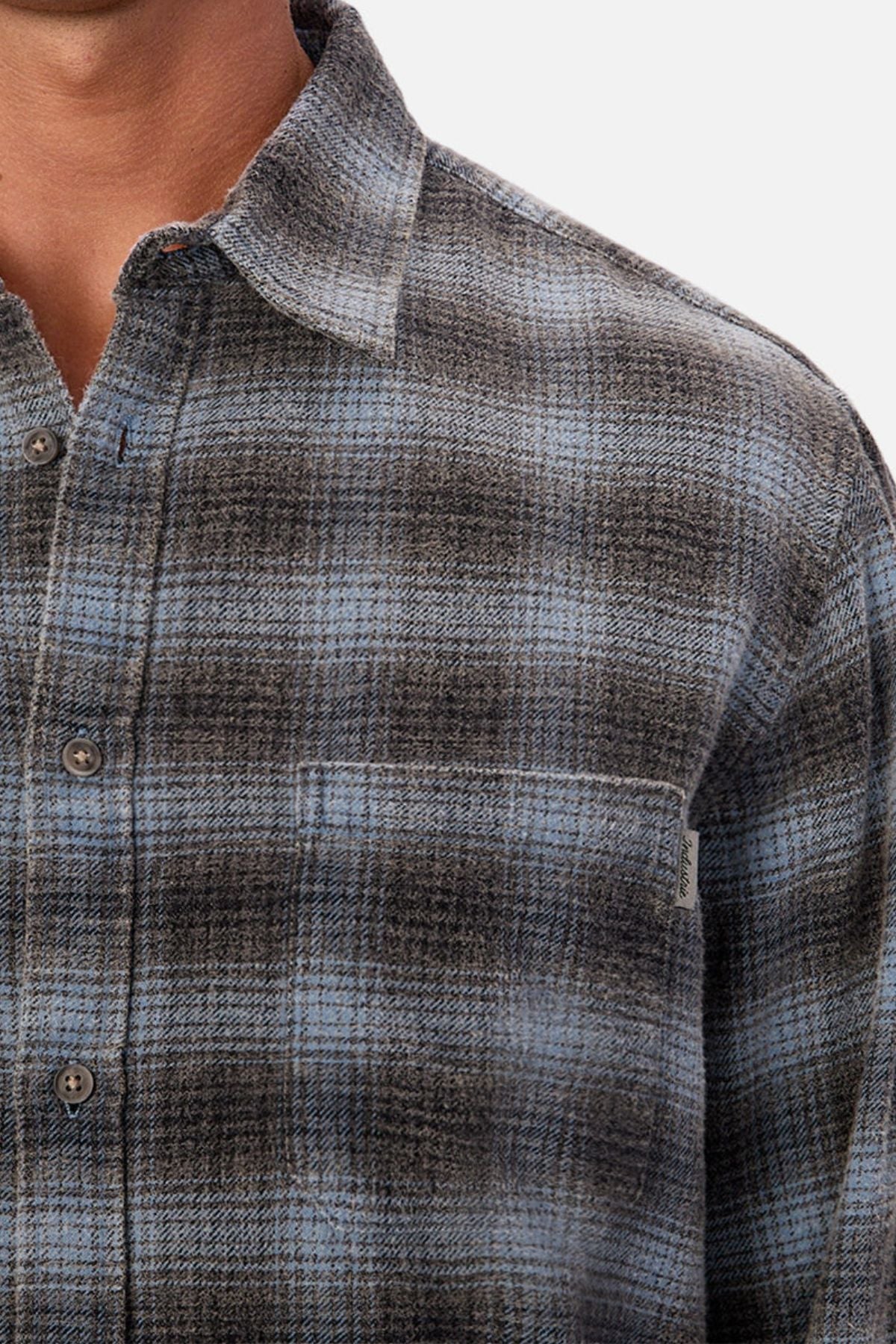 A close-up of a person wearing the Industrie Durango Long Sleeve Shirt, featuring a gray and blue plaid pattern. The image highlights the upper chest, collar, and left arm, showcasing this cotton wardrobe essential.